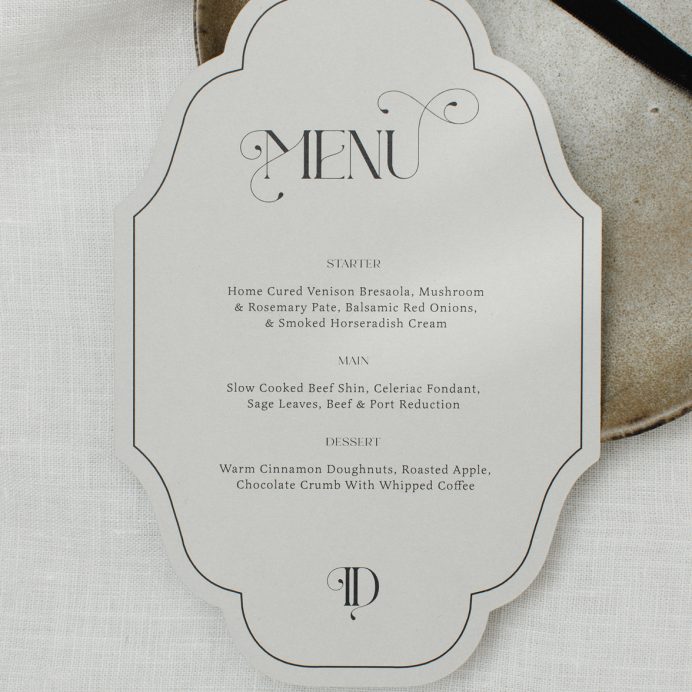 Vintage inspired cut to shape wedding menu in grey with ornate font.