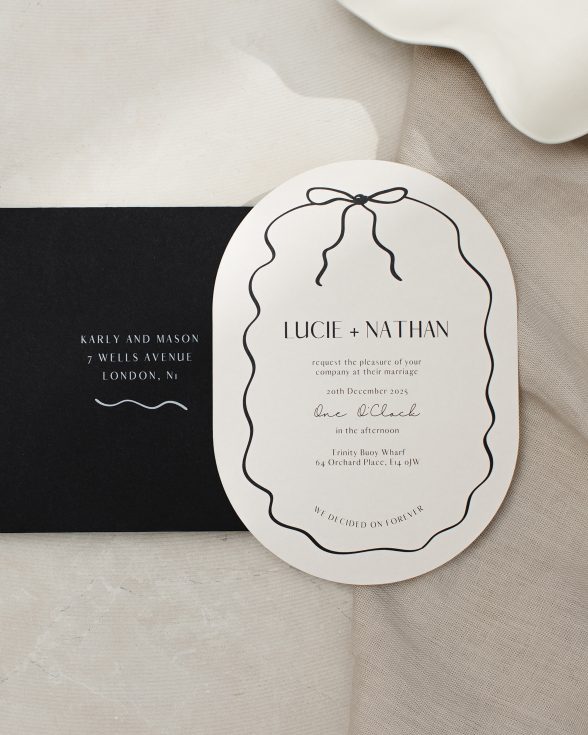 Double arch shape almond and black wedding invitation with hand drawn squiggly line border and bow. Black envelope with white ink