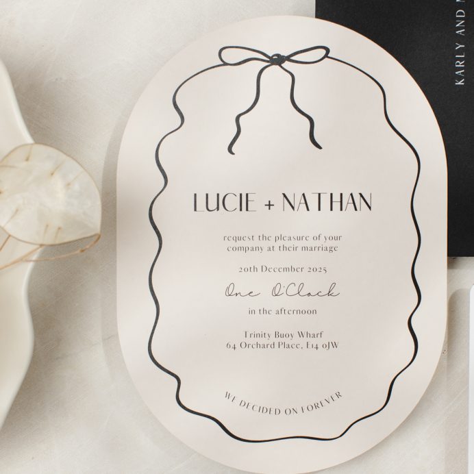 Double arch shape almond and black wedding invitation with hand drawn squiggly line border and bow. Black envelope with white ink