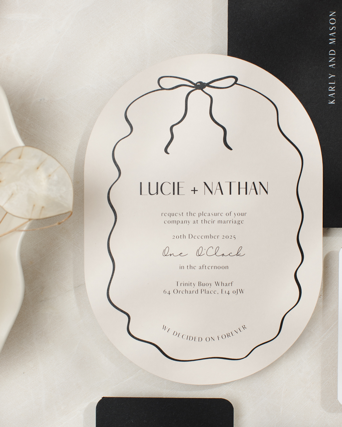 Double arch shape almond and black wedding invitation with hand drawn squiggly line border and bow. Black envelope with white ink